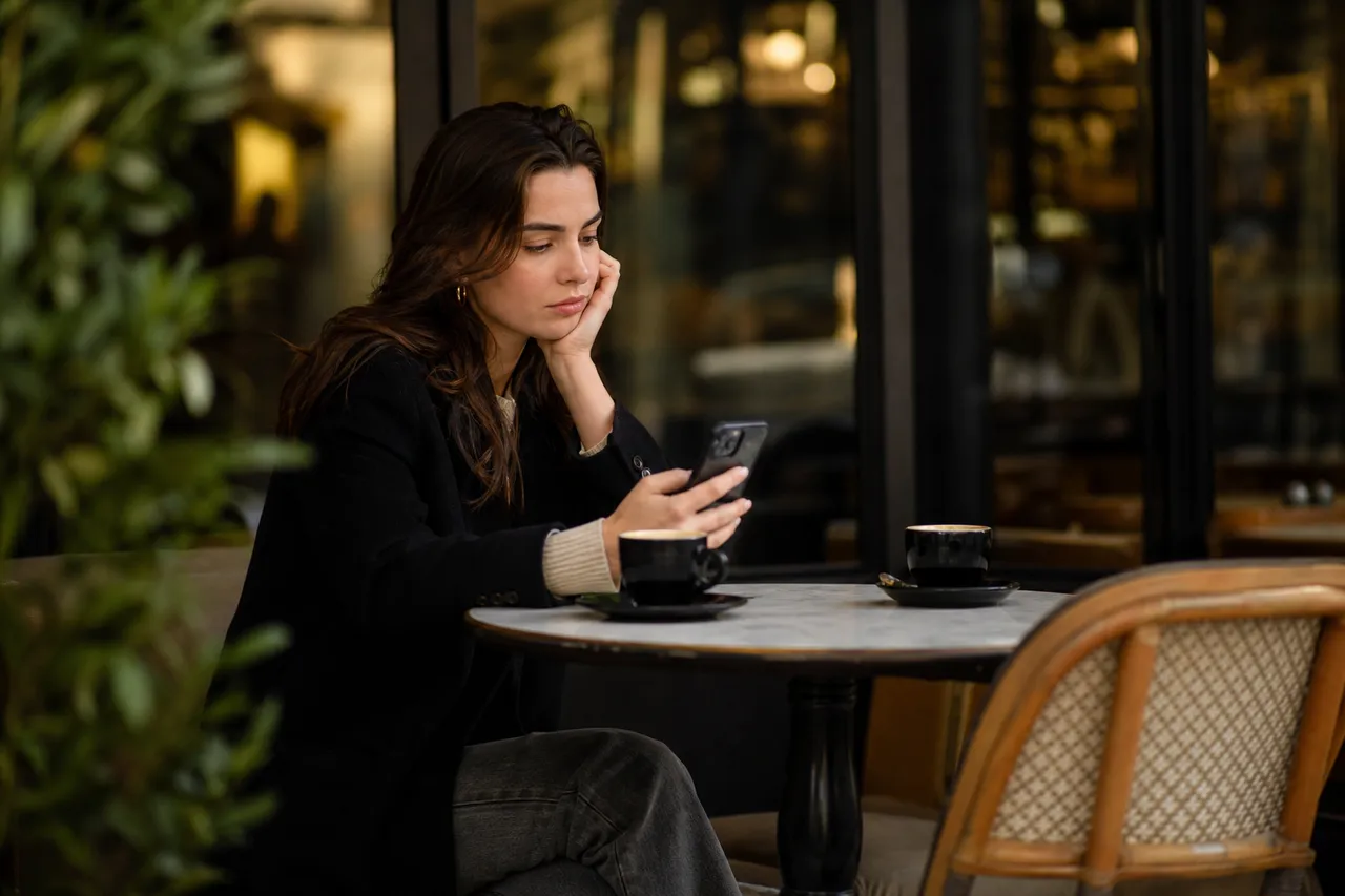 Personne regardant son téléphone sans nouvelle réponse, assise seule à une table de café